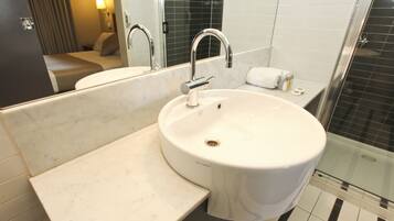 Un baño con un lavabo blanco, un espejo, una ducha y una toalla sobre el mostrador.