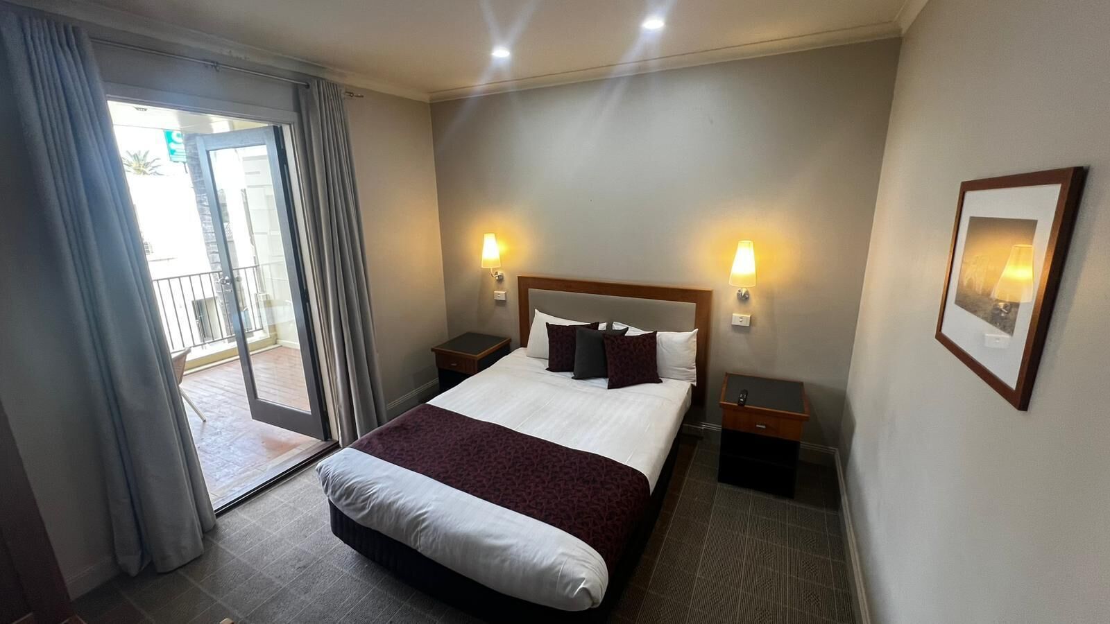 A hotel room with a bed, two bedside tables, a window with curtains, and a framed picture on the wall.
