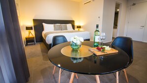 Een hotelkamer met een bed, nachtkastje, lamp en een eettafel met stoelen.