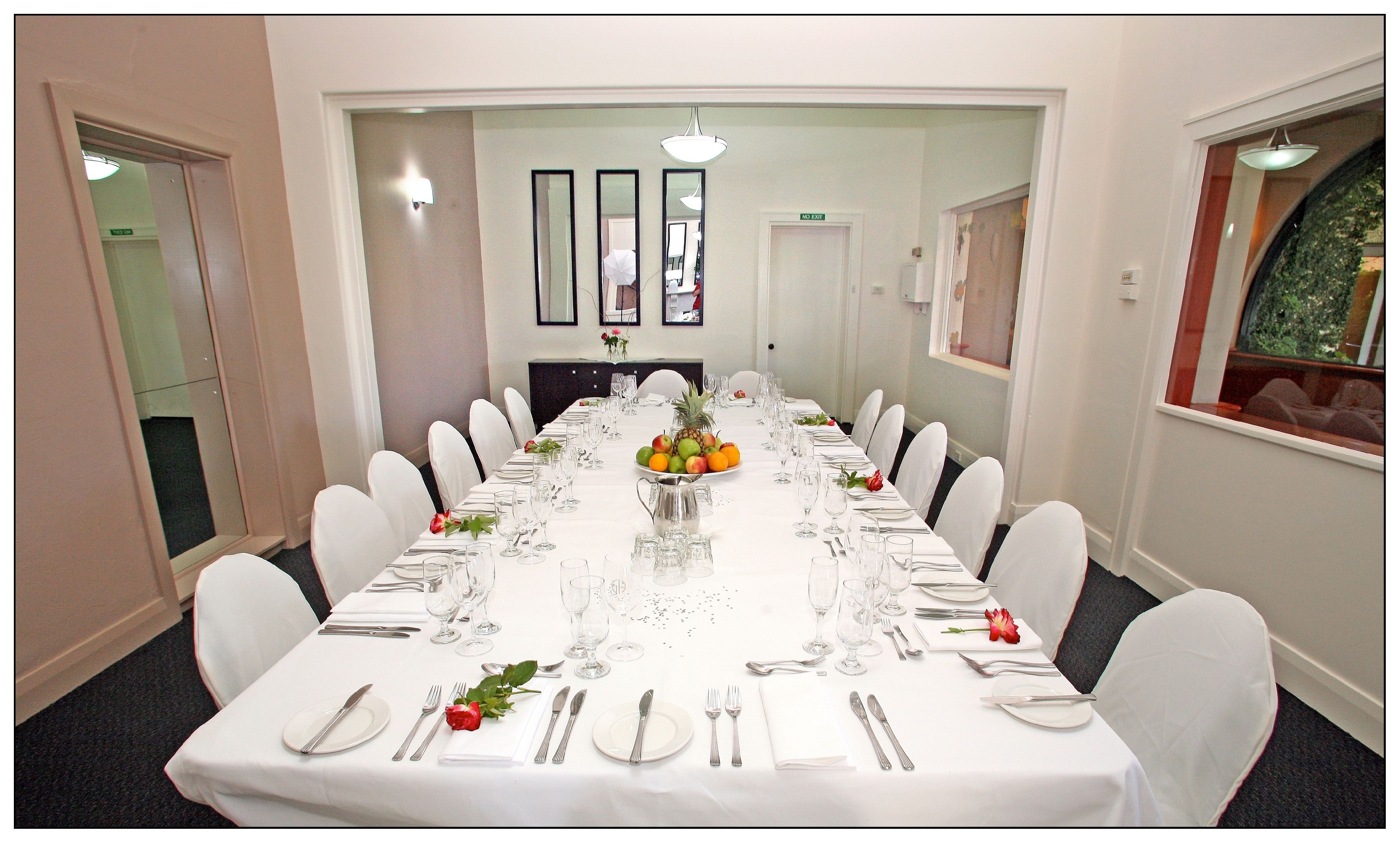 A long dining table set with white tablecloth, chairs, and a fruit centerpiece.