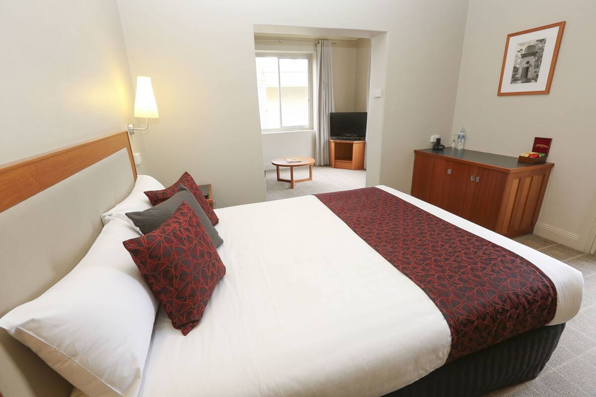 Une chambre d’hôtel avec un lit, un bureau, une télévision et un tableau encadré au mur.