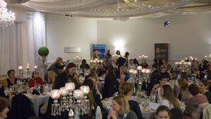 Een formeel evenement met ronde tafels, kaarsen, glazen en borden.