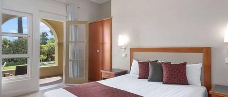 Ein Hotelzimmer mit einem großen Bett, einem Schreibtisch, einem Stuhl, einem Kleiderschrank und einer Tür, die auf einen Balkon führt.