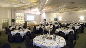 Een balzaal met ronde tafels gedekt voor een formeel evenement, met kroonluchters en gordijnen.
