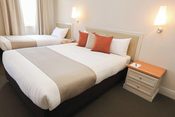 Une chambre d’hôtel avec deux lits, une table de chevet avec une lampe et un téléphone fixé au mur.