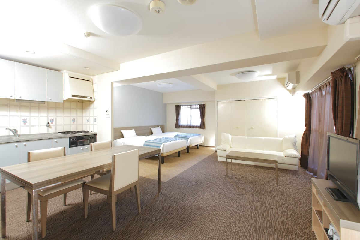 Habitación de hotel compacta con kitchenette, una cama, un sofá, un televisor y una zona de comedor.