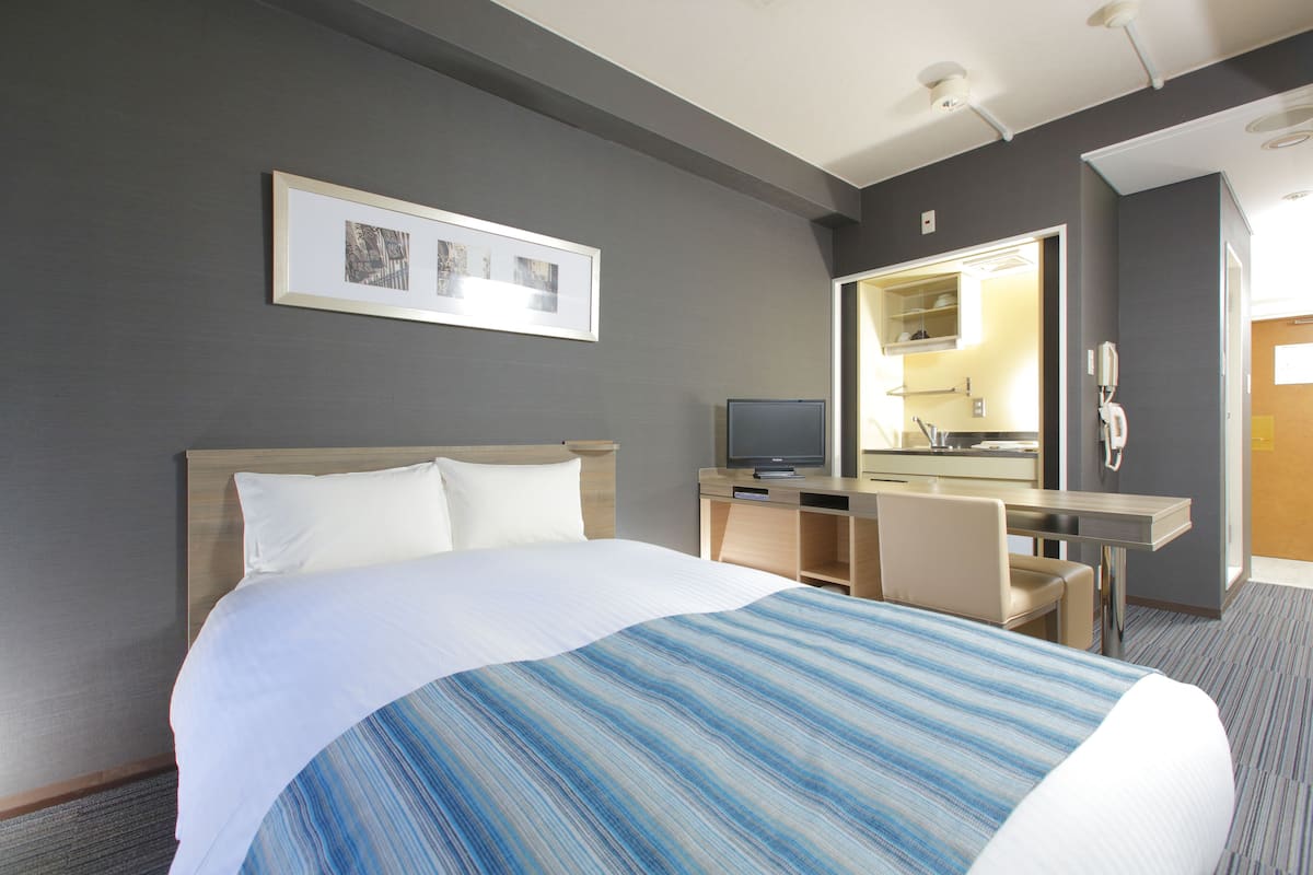 Habitación de hotel con una cama grande, un escritorio con computadora, un espejo y una pequeña kitchenette.