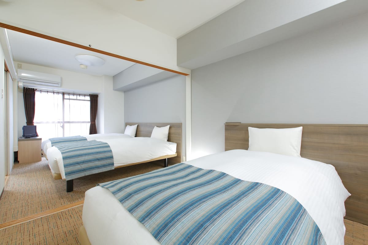 Habitación de hotel con dos camas, un escritorio y una ventana con cortinas.