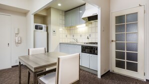 Cocina compacta con microondas, estufa y alacenas. Hay una mesa de comedor con sillas y una puerta con paneles de vidrio esmerilado.
