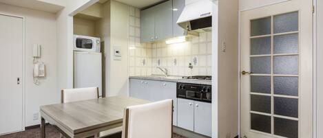 Cocina compacta con microondas, estufa y alacenas. Hay una mesa de comedor con sillas y una puerta con paneles de vidrio esmerilado.