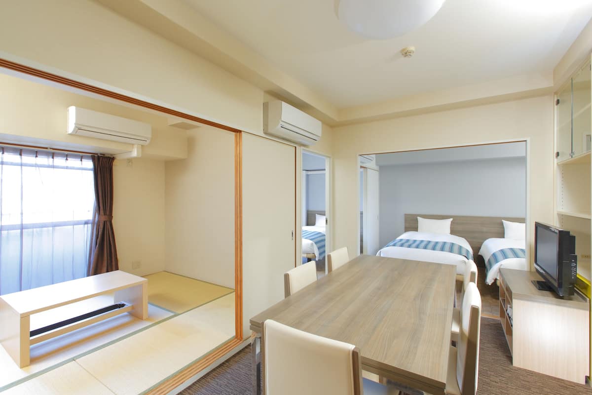 Una habitación de hotel con una mesa de madera, dos camas con ropa de cama a rayas, un televisor y un pequeño escritorio.