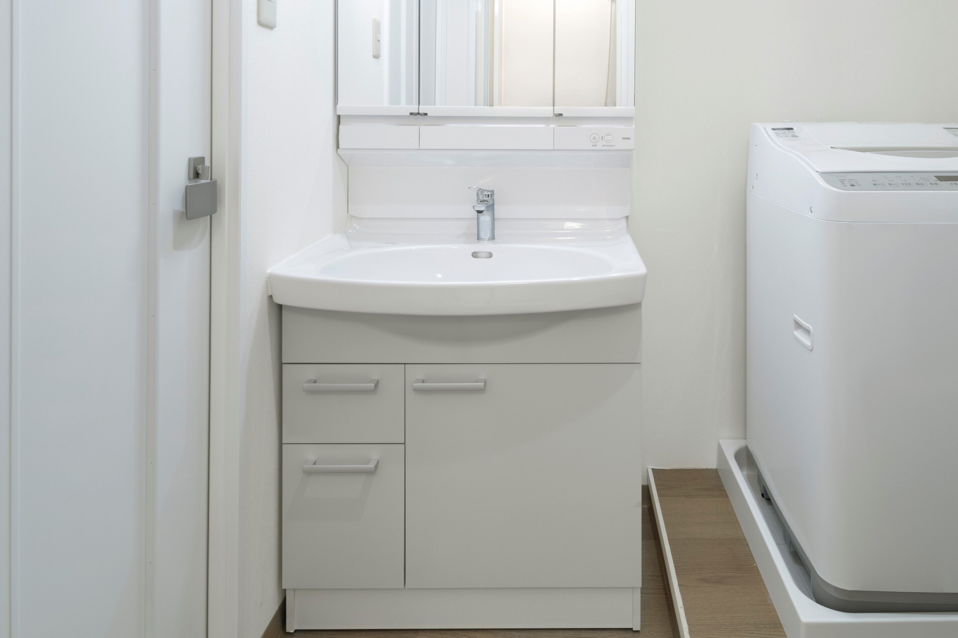 Un baño con un lavamanos blanco, un espejo y una lavadora blanca.