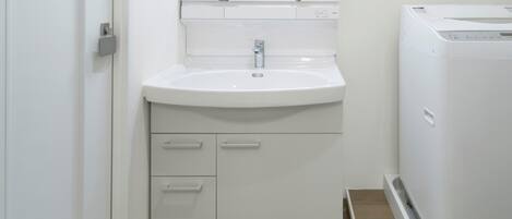 Un baño con un lavamanos blanco, un espejo y una lavadora blanca.