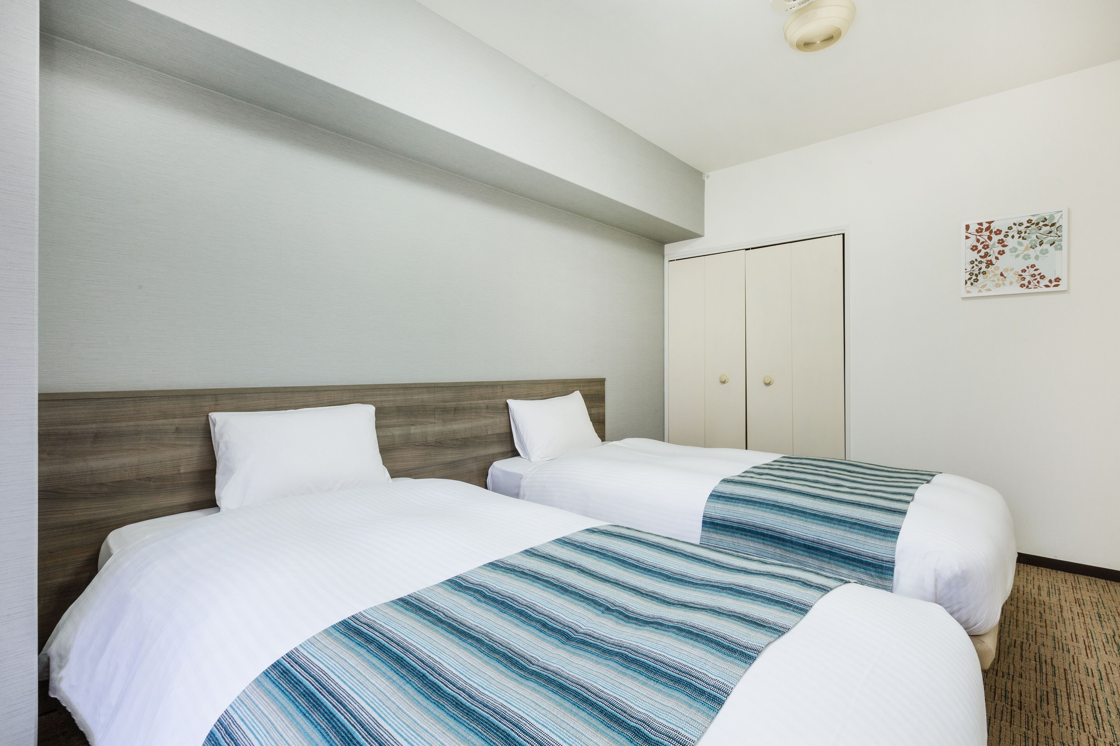 A hotel room with two beds, a wooden headboard, a wardrobe, and a wall-mounted artwork.