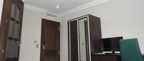 Un dormitorio con cama, armario, televisor y escritorio.