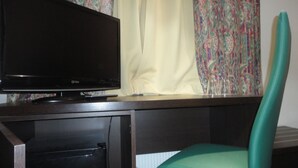 Un televisor sobre un escritorio de madera, una silla verde, cortinas y una pared con estampado.