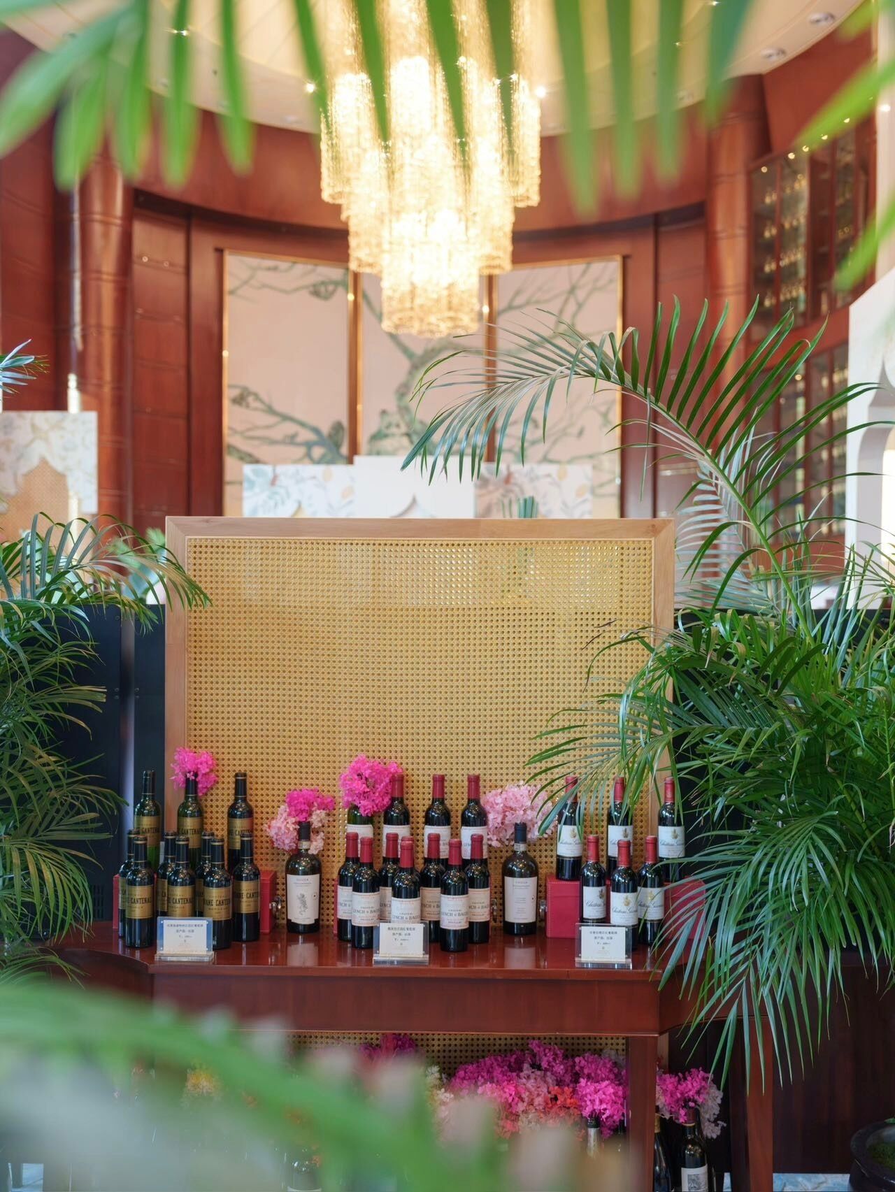Une présentation de vins avec des bouteilles et des fleurs roses, le tout entouré de plantes en pot.