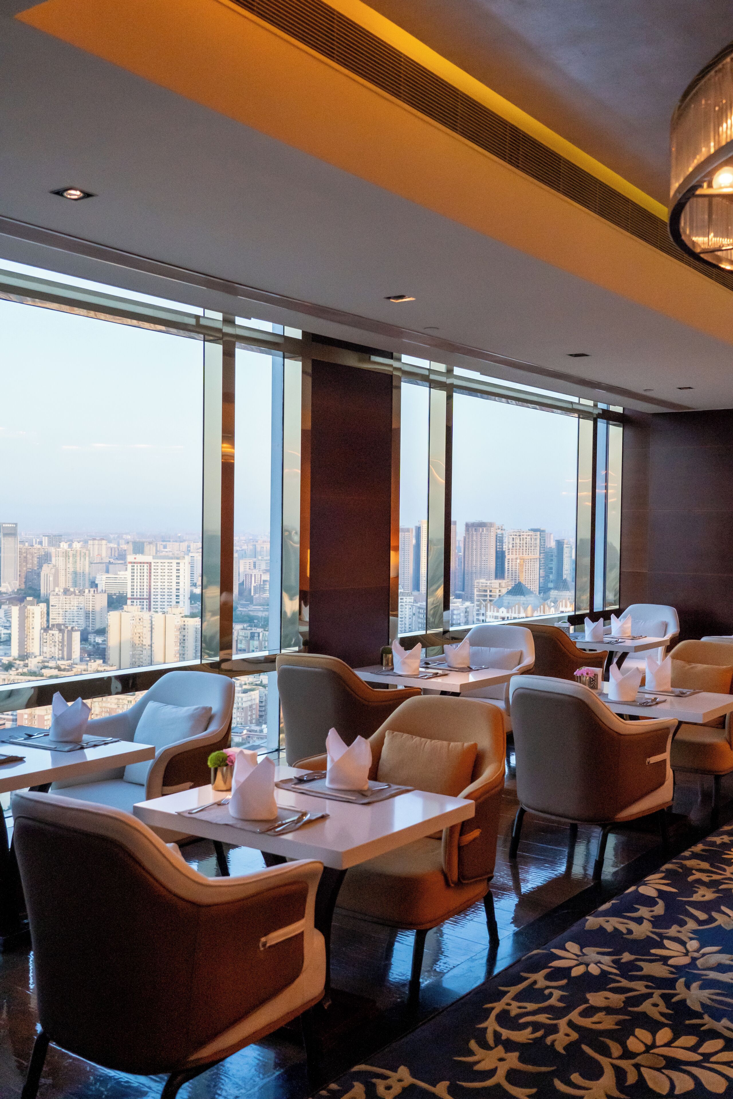 A modern hotel dining area with tables and chairs, large windows offering a city view.