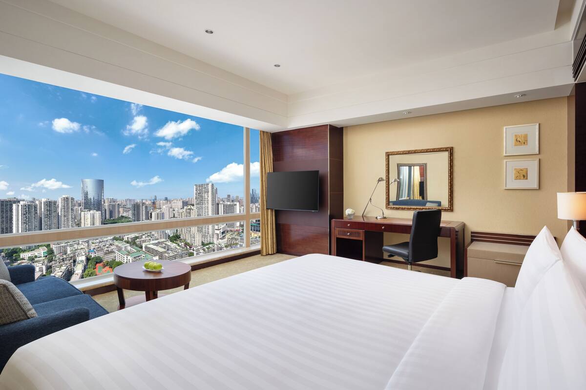 Habitación de hotel con una cama grande, un escritorio, una silla, un televisor y vistas de la ciudad.