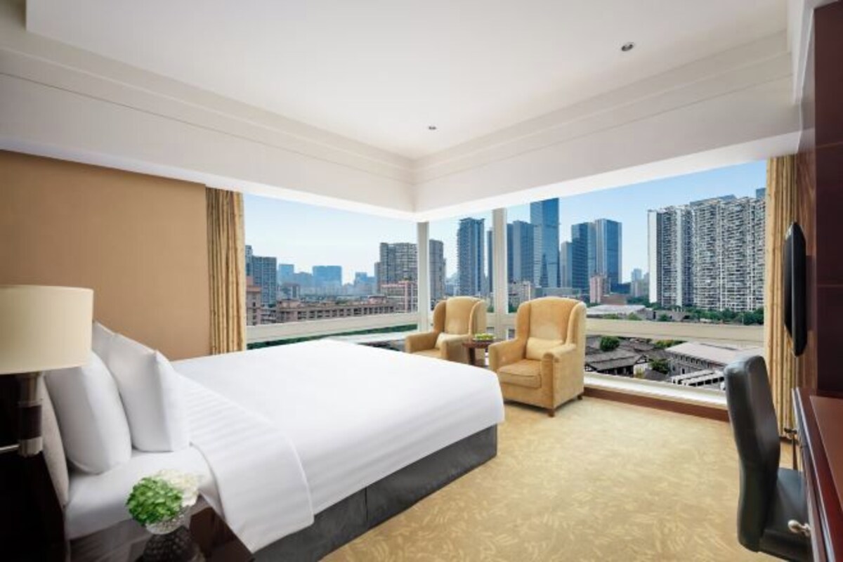 Habitación de hotel con una cama grande, dos sillones, un escritorio y vistas a la ciudad.