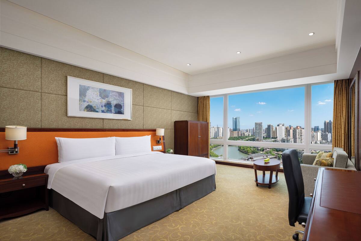 Habitación de hotel con una cama grande, un escritorio, una silla, vistas a la ciudad y una ventana con cortinas.