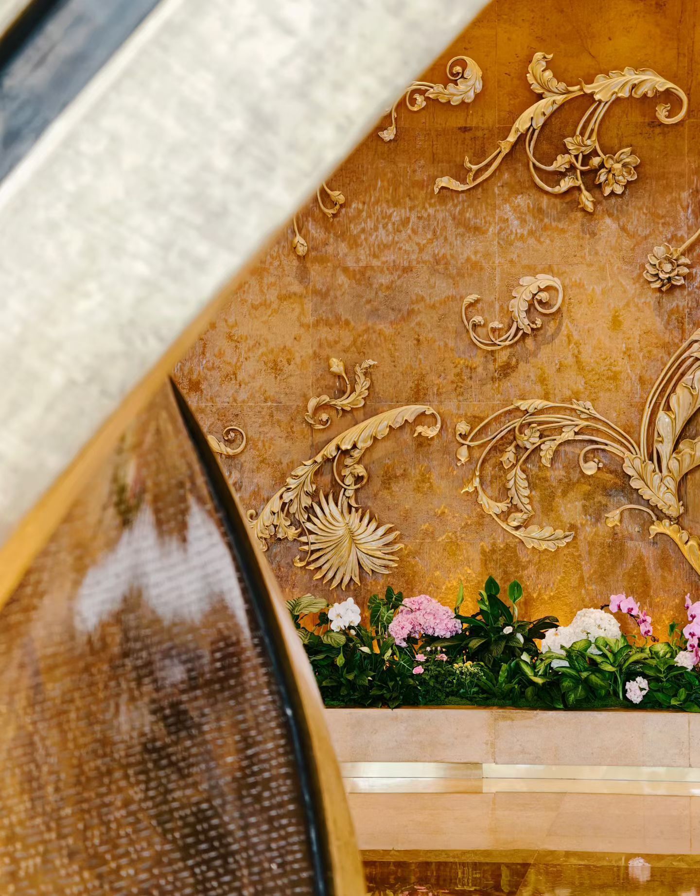 A close-up of a decorative wall with intricate golden designs and a floral arrangement at the bottom.