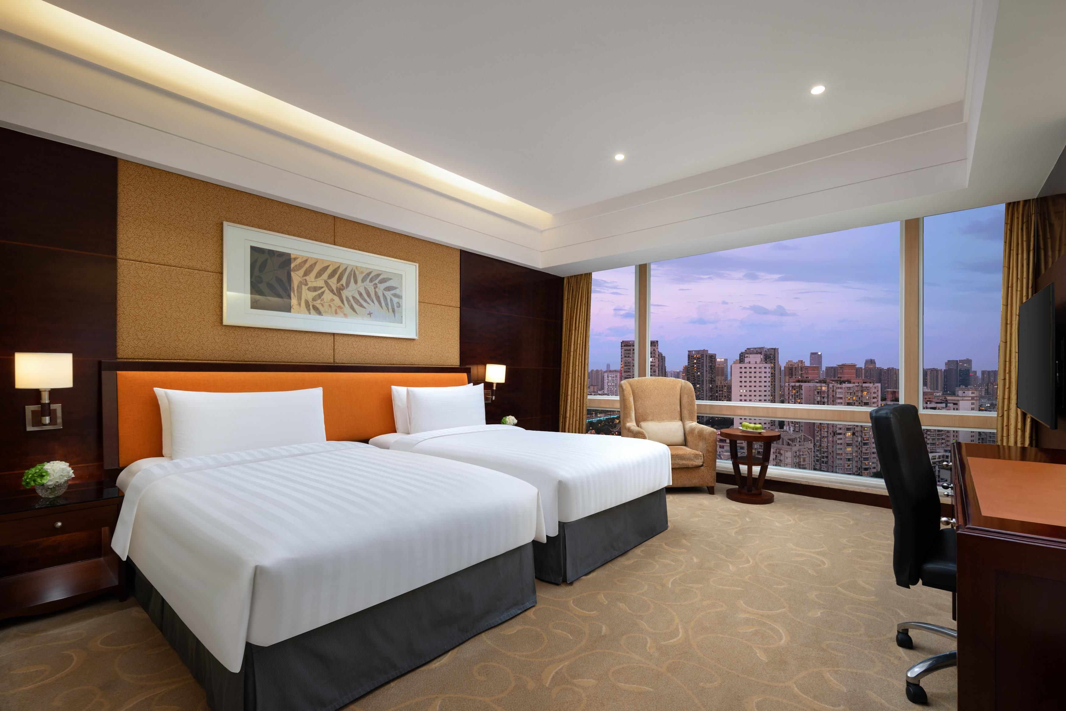 Une chambre d’hôtel avec deux lits, un bureau, une chaise, une vue sur la ville et une grande fenêtre.