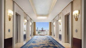 A hotel corridor with a blue carpet, light fixtures, and a view of a cityscape through a window. - Shangri-La Chengdu (Chengdu)