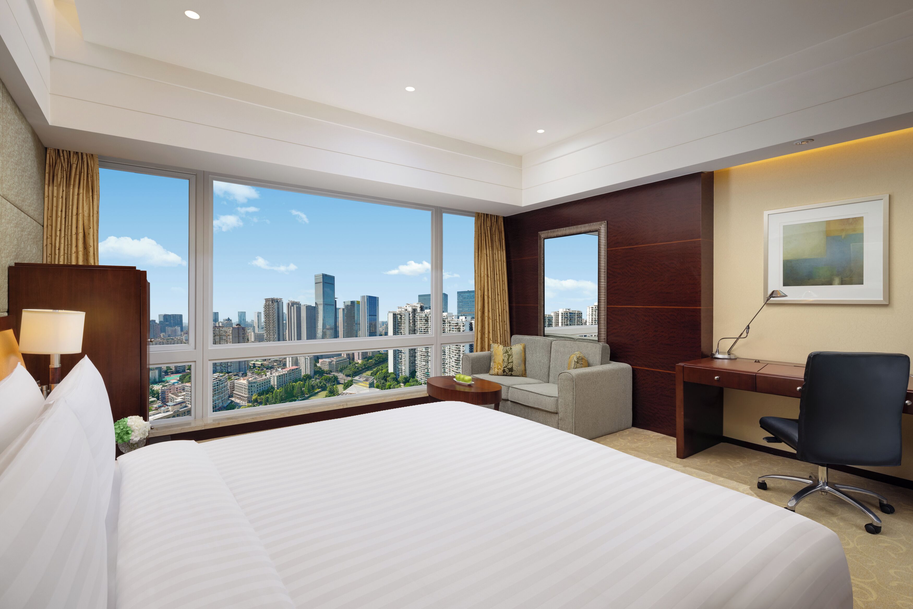 A hotel room with a large bed, a desk, a chair, and a view of the cityscape.