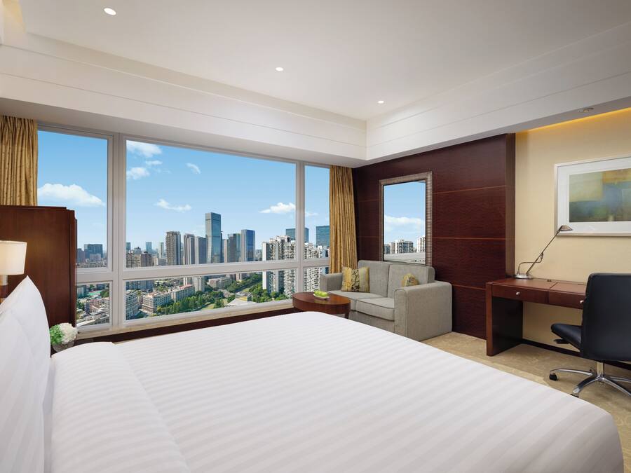 A hotel room with a large bed, a desk, a chair, and a view of the cityscape.