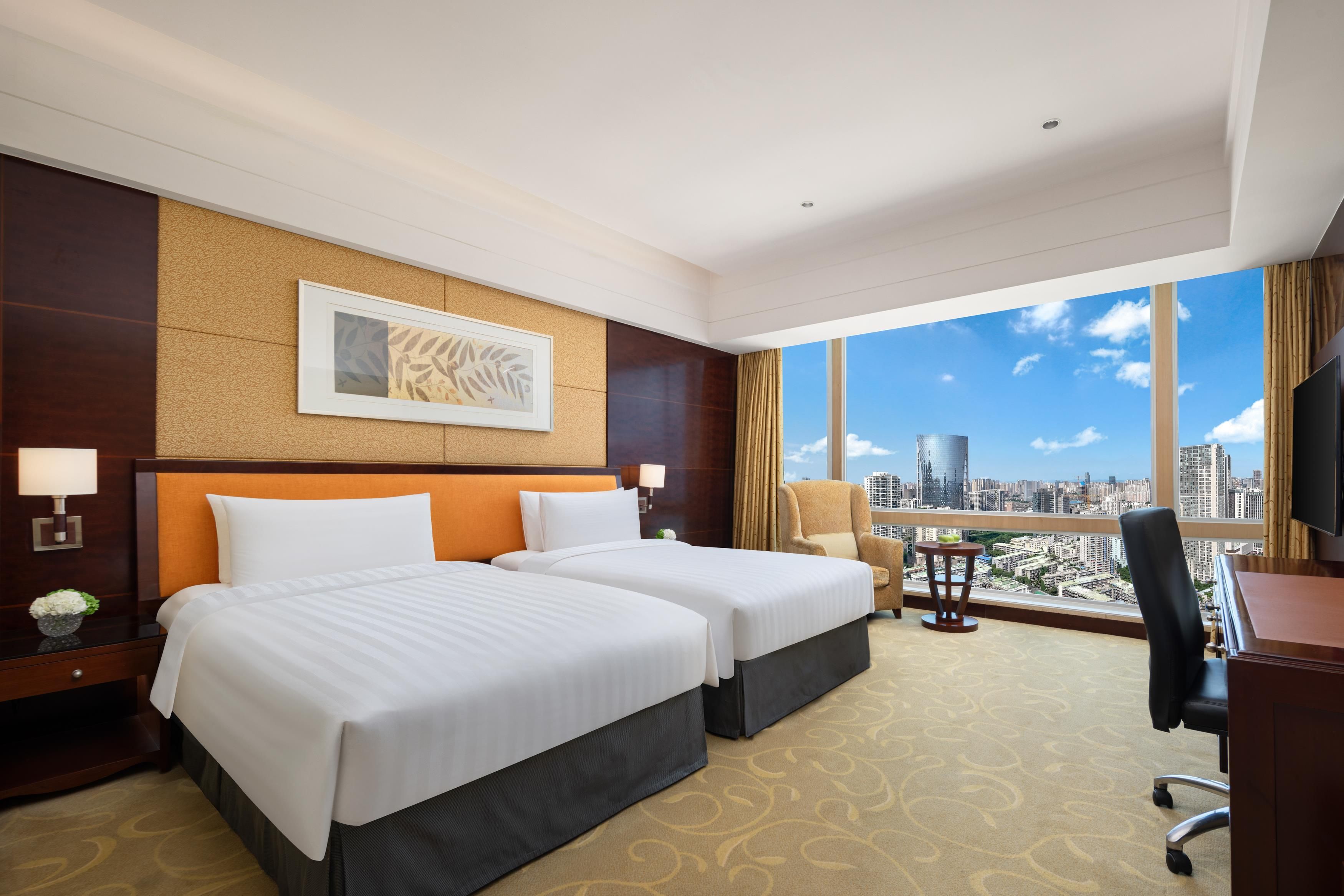 Habitación de hotel con dos camas, un ventanal con vistas a la ciudad, un escritorio y una silla.