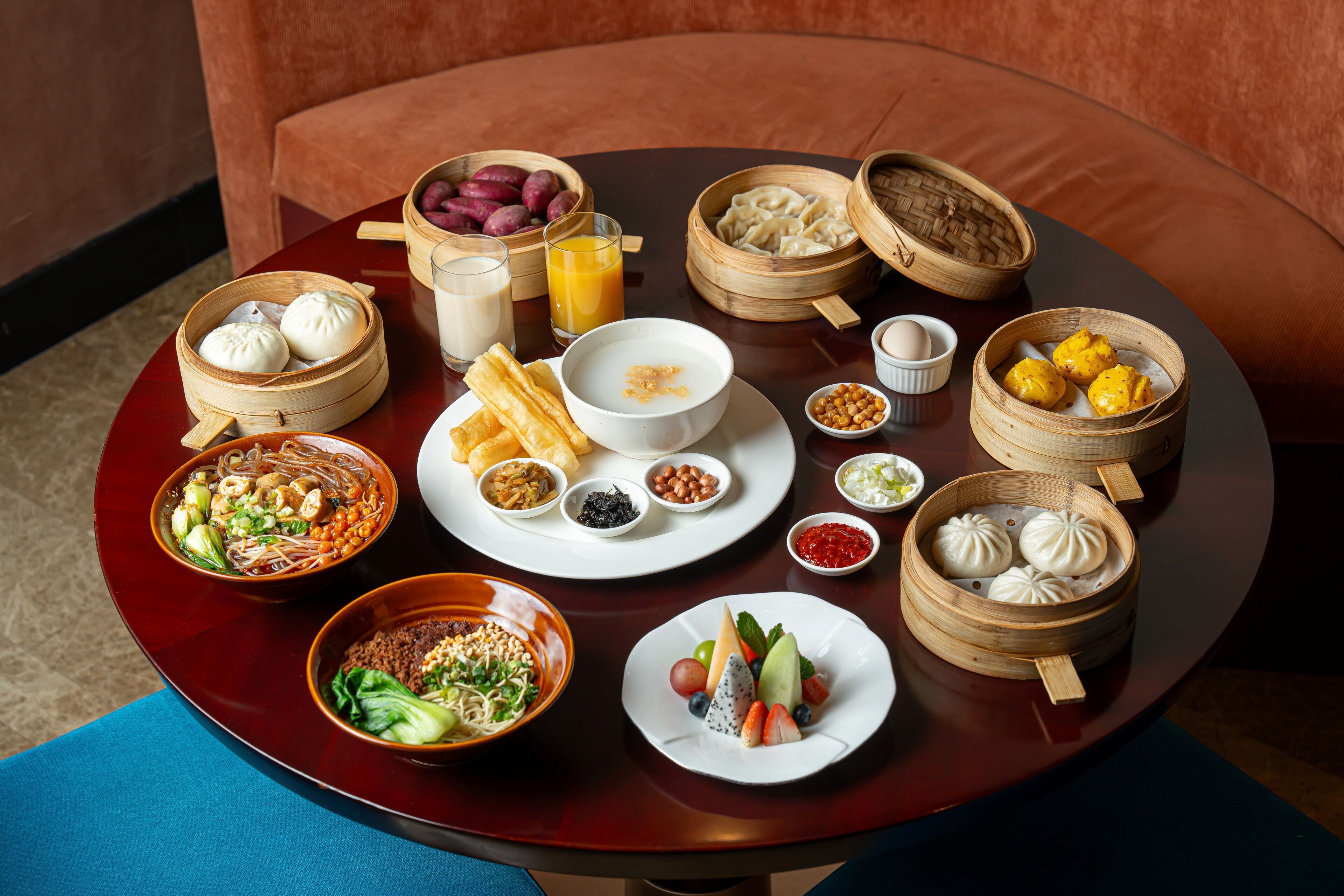 A round table with various dishes including dumplings, noodles, and fruit.