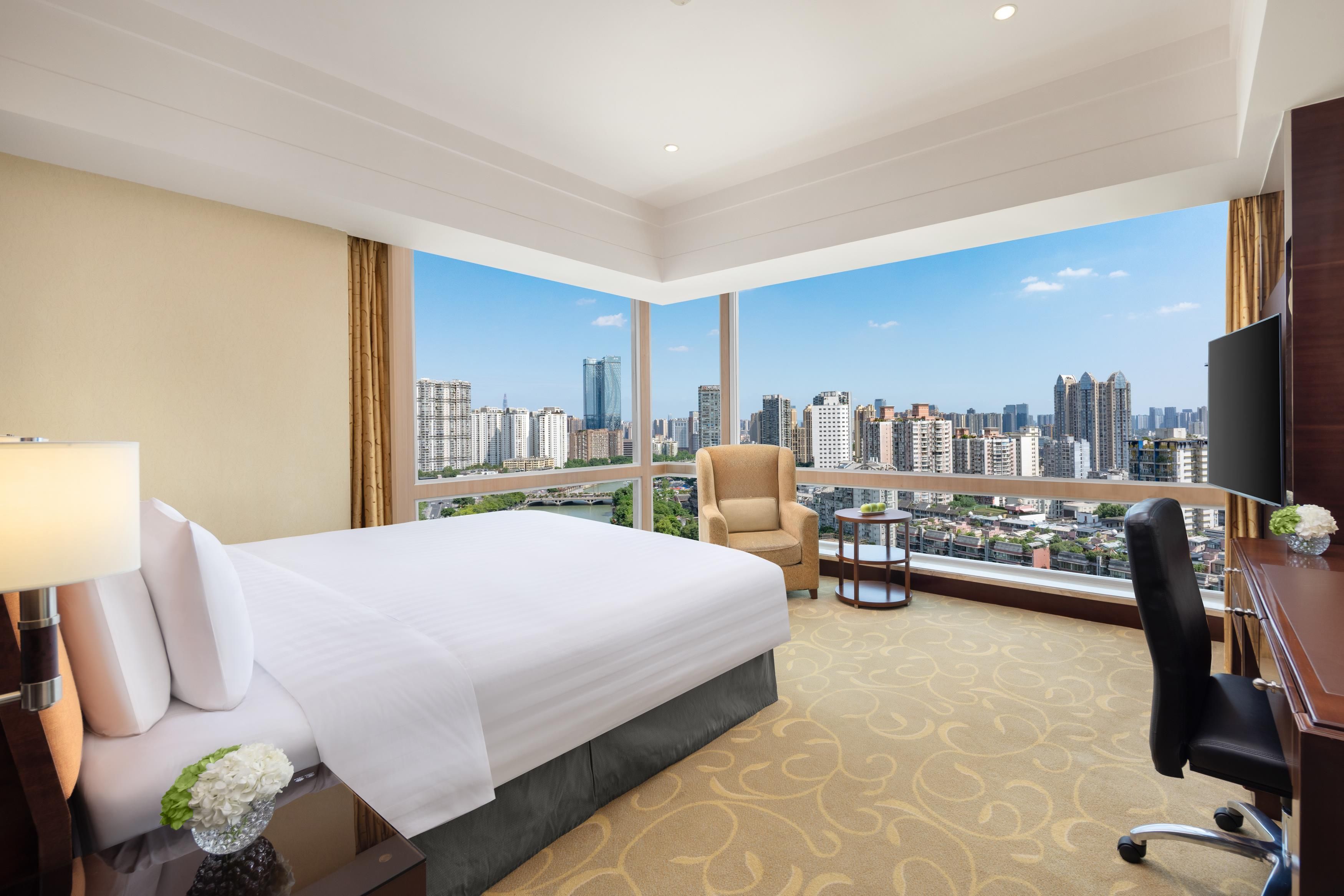 A hotel room with a large bed, a chair, a desk, and a view of a cityscape.