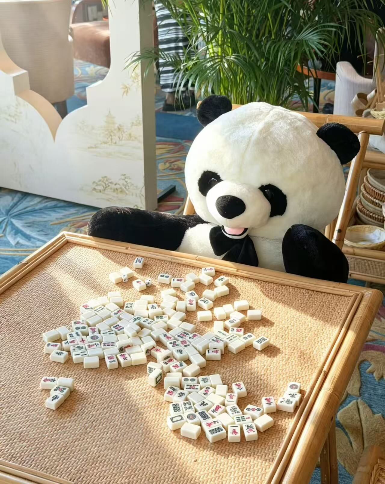 Un peluche de panda sentado sobre un tapete tejido con fichas de mahjong dispersas alrededor.