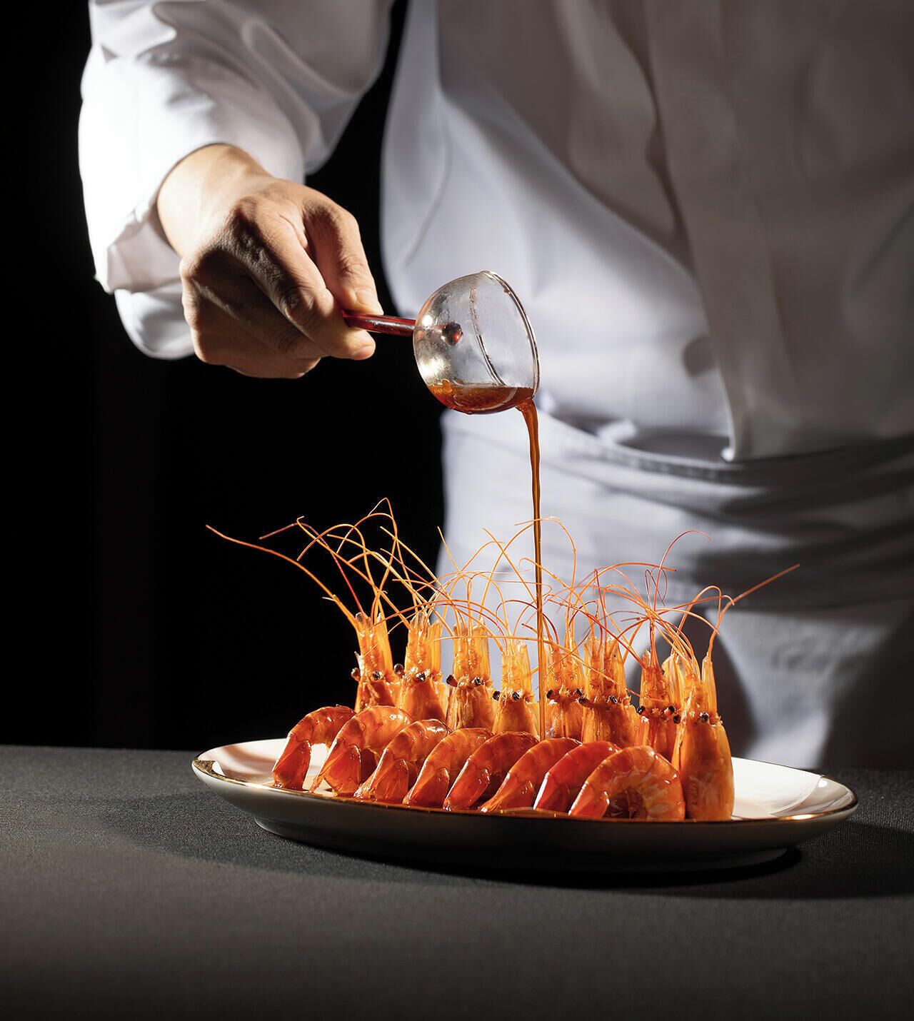 A chef pouring sauce over a dish of cooked shrimp.