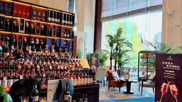 A bar area with a variety of liquor bottles and glasses, a chandelier, and a large window with a view of greenery.
