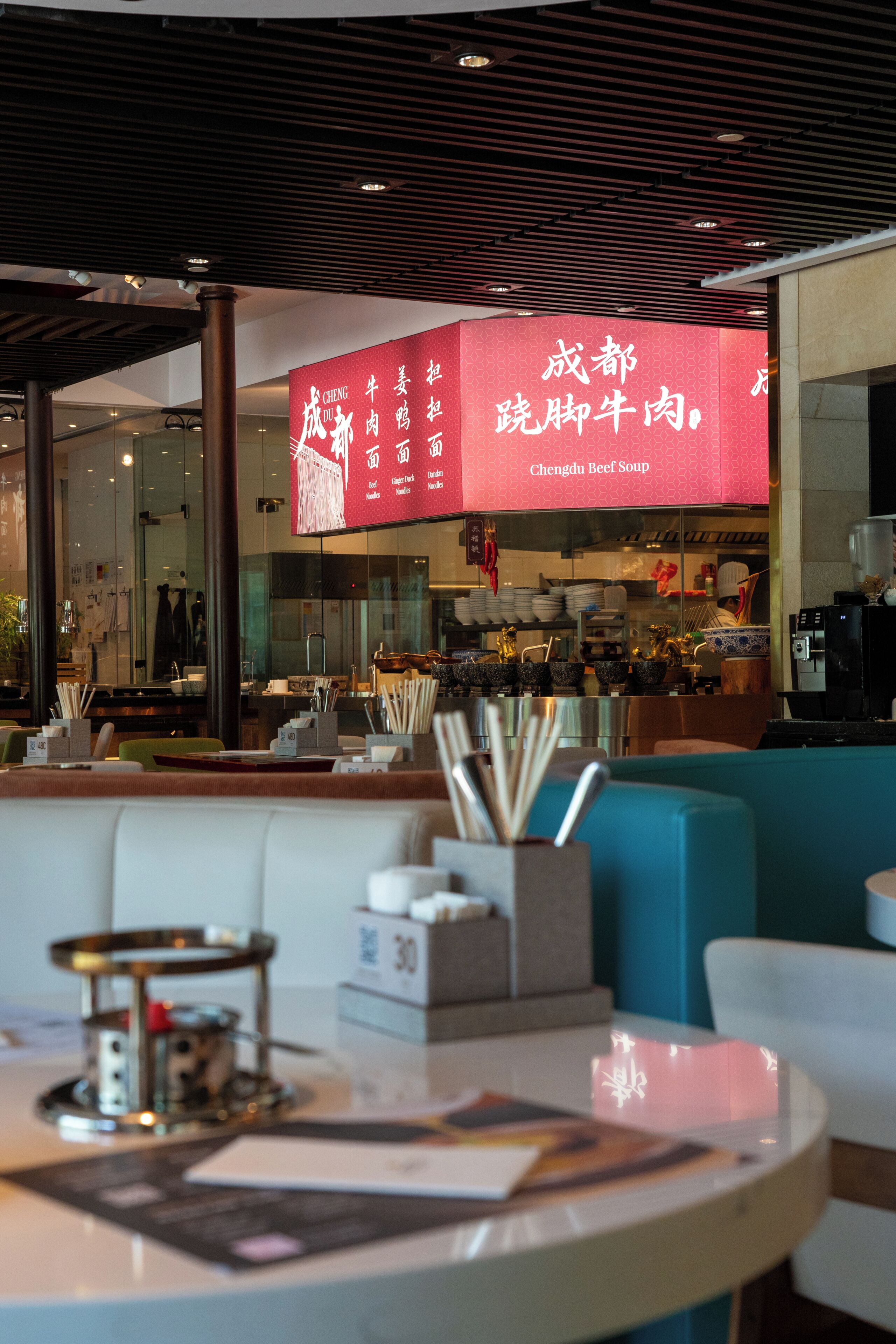 A restaurant interior with a red menu board, seating area, and kitchen in the background.