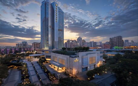 A high-rise building with a modern glass facade, surrounded by a landscaped area with trees and a well-lit parking lot.