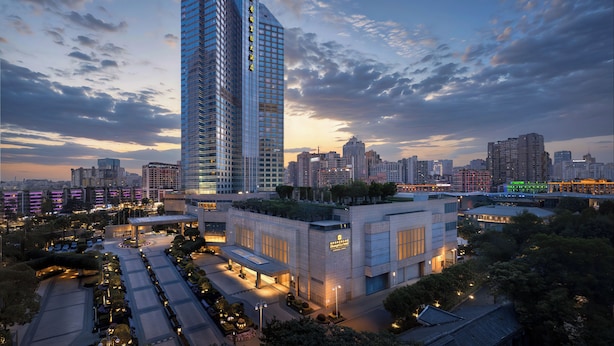 A high-rise building with a modern glass facade, surrounded by a landscaped area with trees and a well-lit parking lot. - Shangri-La Chengdu (Chengdu)