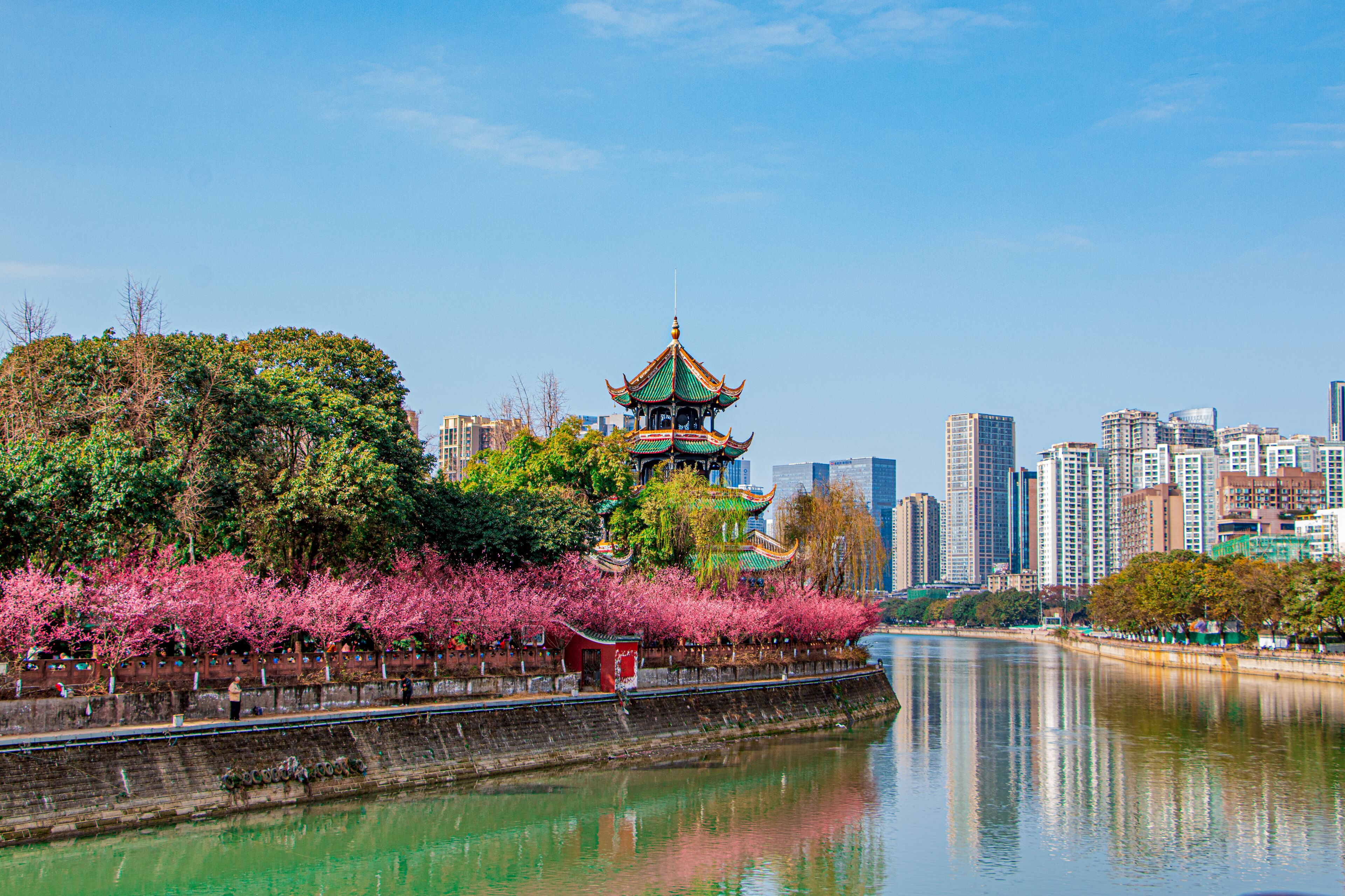 A traditional pagoda with a river in the foreground and a modern cityscape in the background.