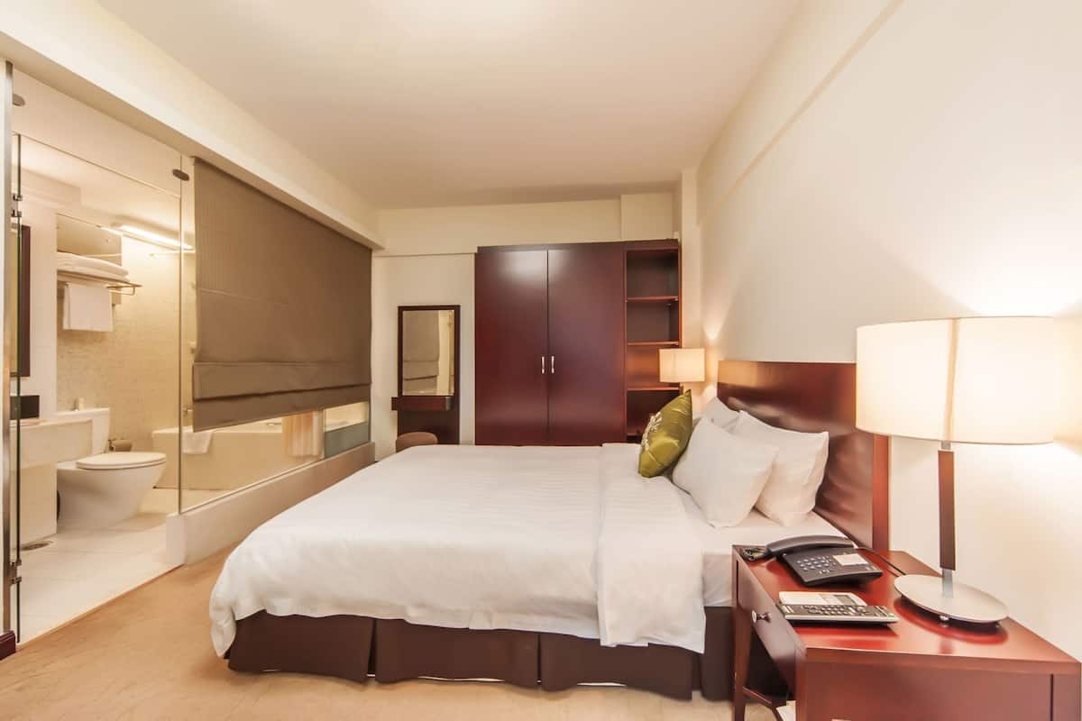 A hotel room with a bed, bedside table, lamp, and a mirror.