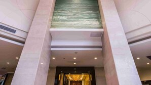 Un hall d’entrée moderne avec un grand lustre, un mur vert à texture et un sol en marbre.
