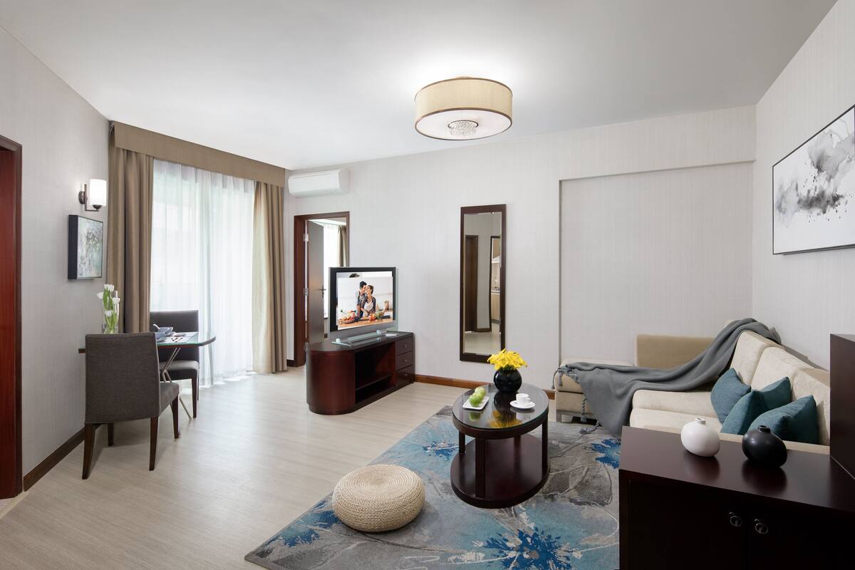A modern living room with a flat-screen TV, a sofa, a coffee table, and a dining area with a table and chairs.