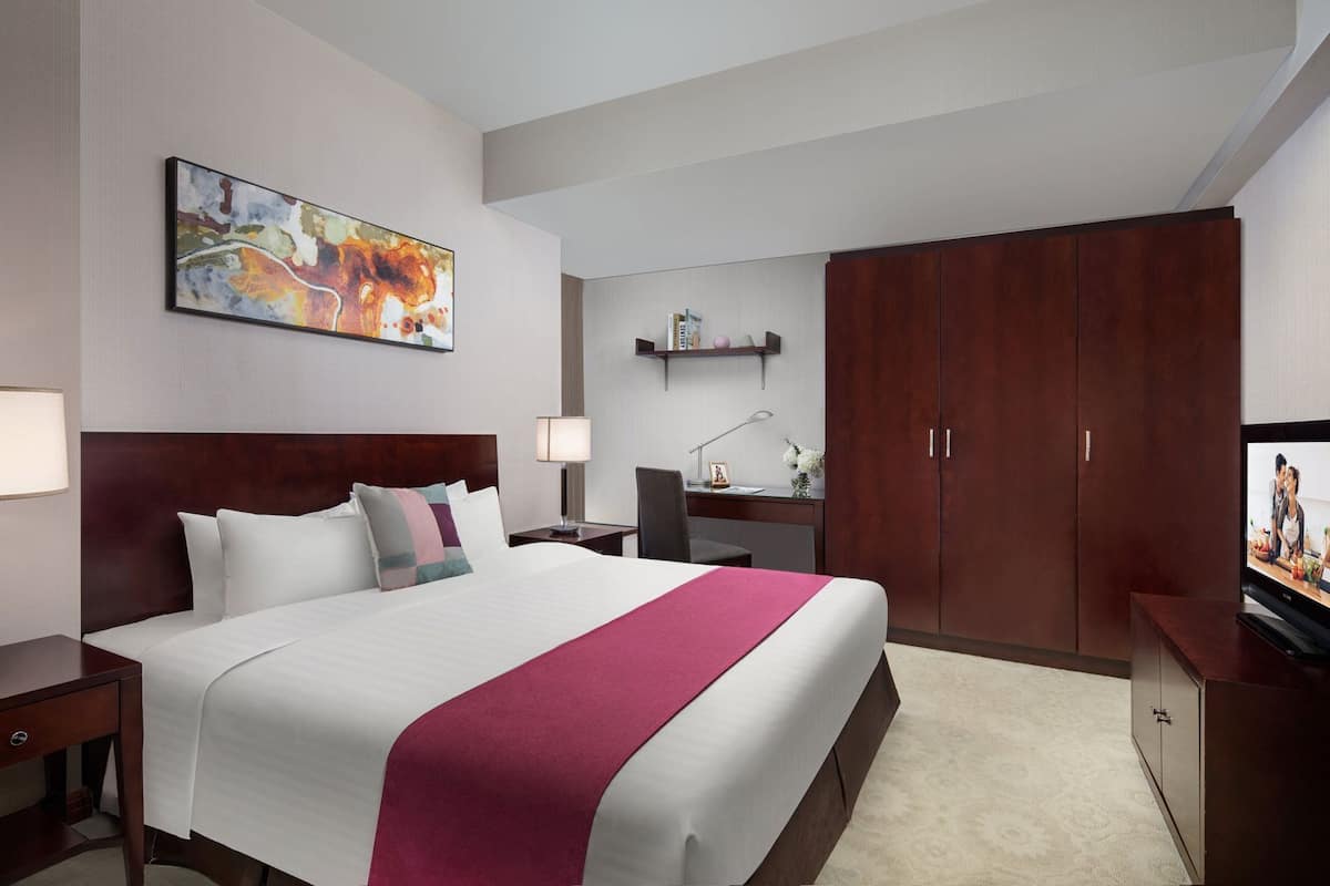 A hotel room with a large bed, a desk, a television, a wardrobe, and a painting on the wall.