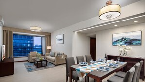 Une chambre d’hôtel moderne dotée d’un coin repas, d’un ensemble de canapés et d’une grande fenêtre offrant une vue sur la ville.
