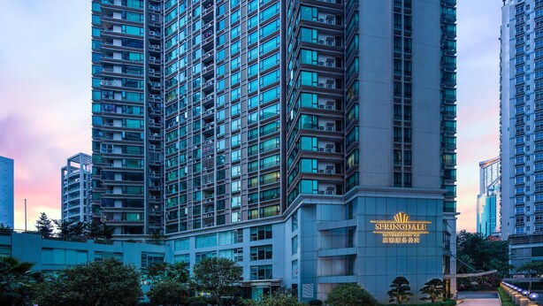 Un immeuble de grande hauteur doté de nombreux balcons, d’un jardin bien entretenu et surplombant un ciel dégagé.