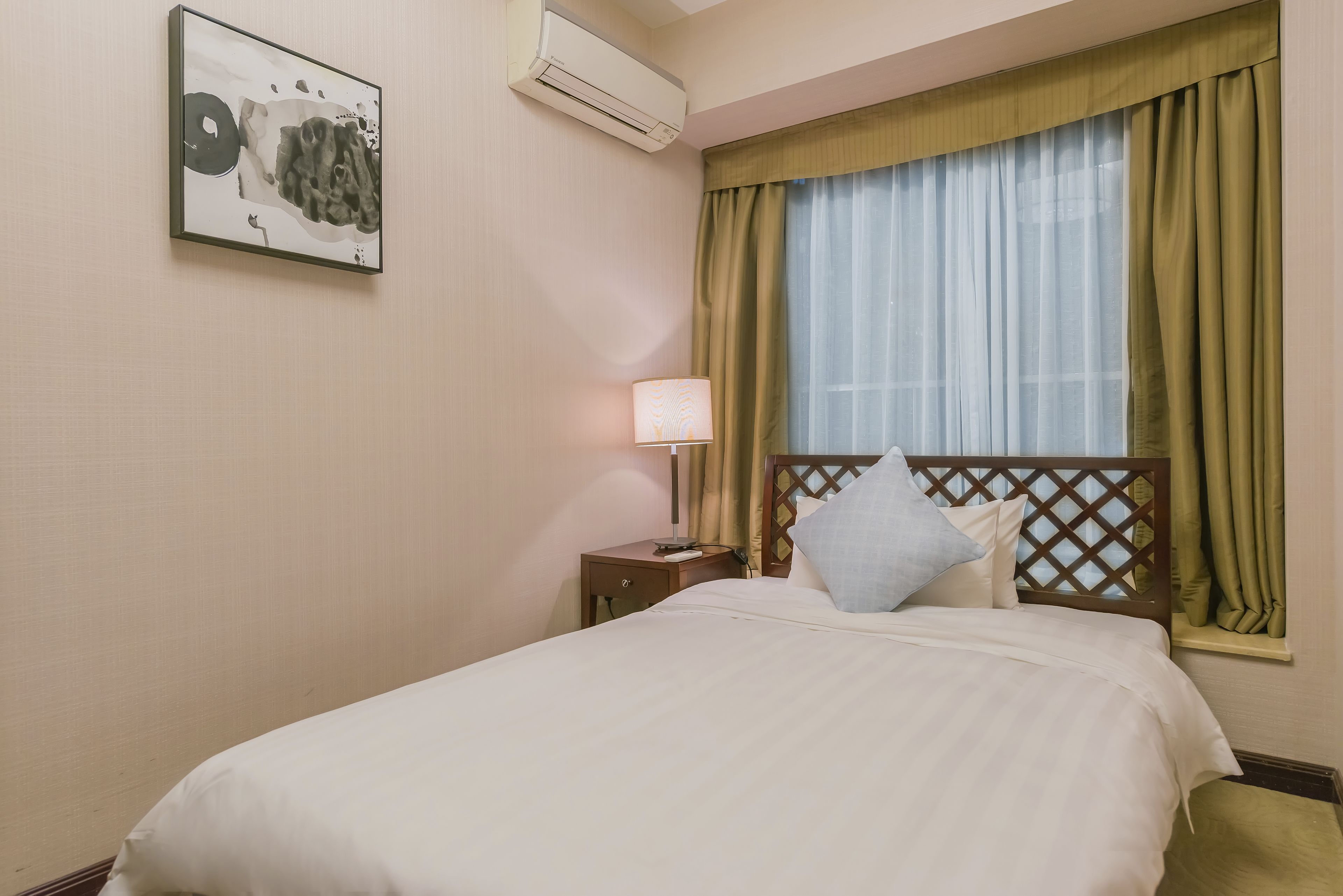 A hotel room with a bed, a nightstand, a lamp, a window with curtains, and an air conditioning unit.