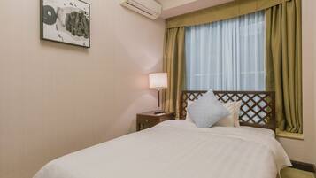 A hotel room with a bed, a nightstand, a lamp, a window with curtains, and an air conditioning unit.