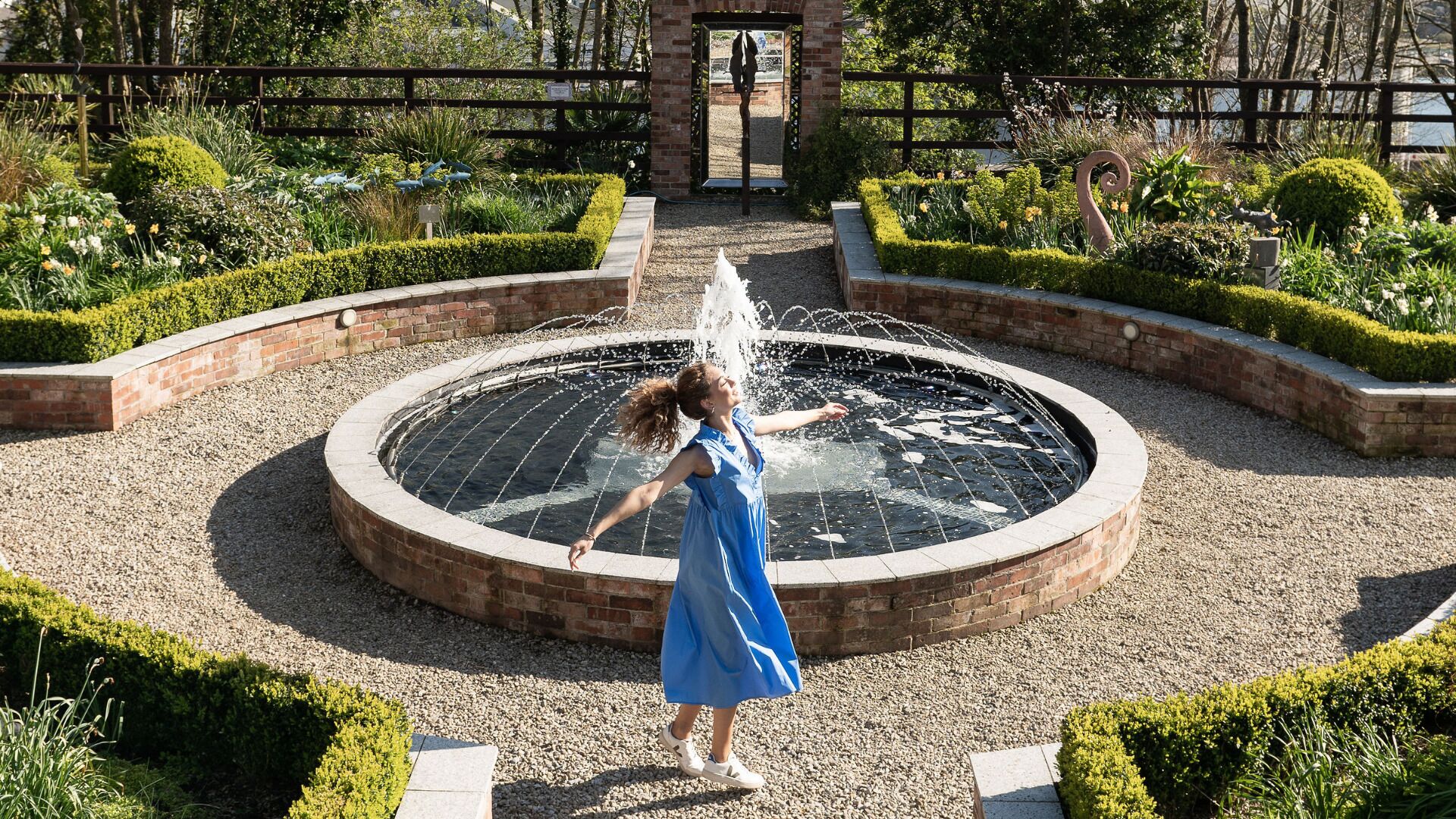 A circular fountain with water jets in the center, surrounded by a brick border and gravel.
