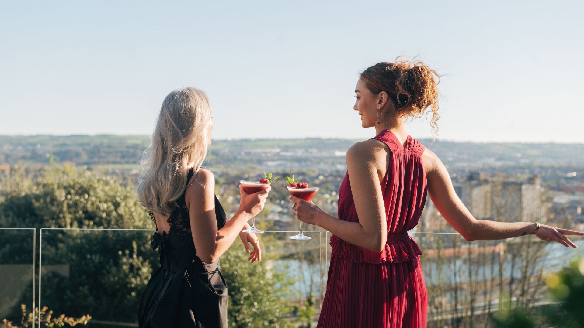 Dos mujeres sosteniendo bebidas con una vista panorámica al fondo.